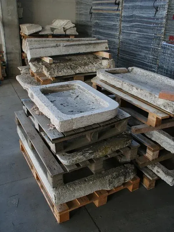 Lavelli in pietra impilati su pallet di legno in un magazzino.