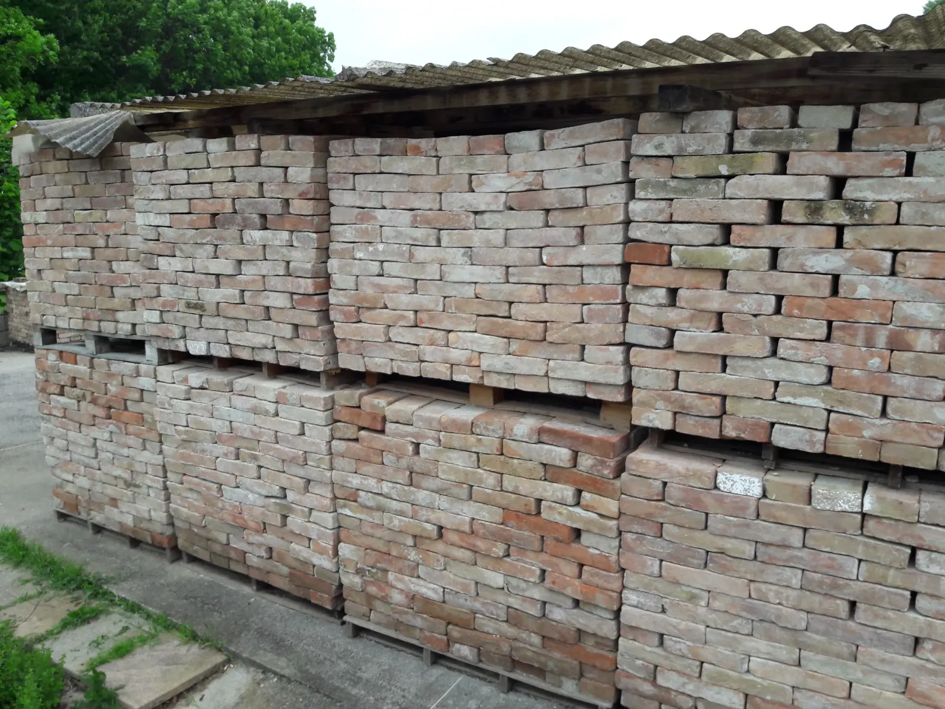 Pile di mattoni rosso-marroni sotto un tetto ondulato in un ambiente esterno.