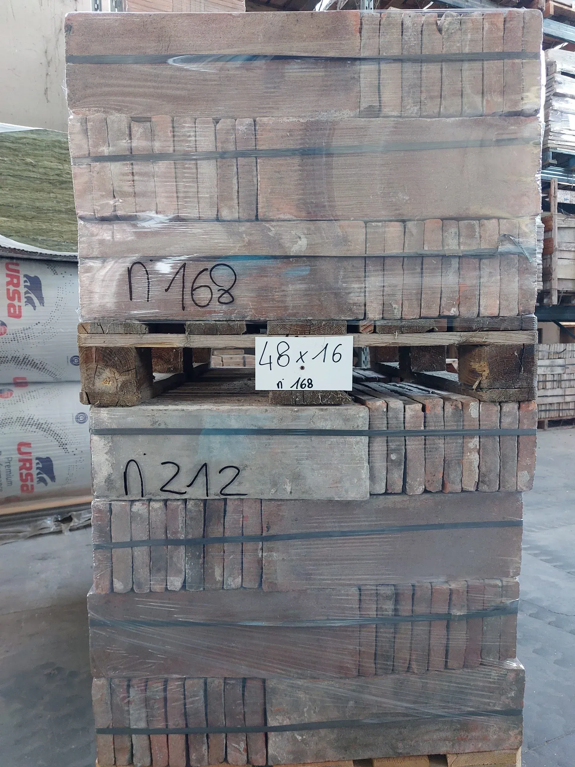 Pila di mattoni marroni avvolti nella plastica su un pallet di legno; numeri scritti sulla confezione.