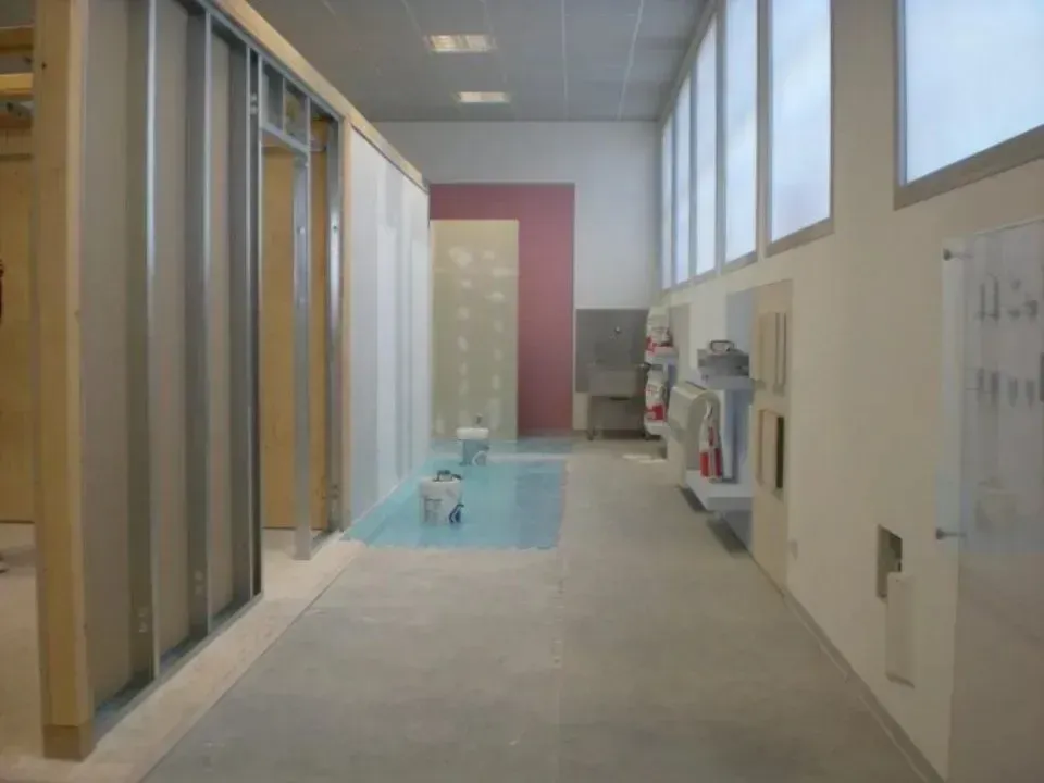 Interno di un cantiere edile; struttura in metallo e legno, pareti grezze e pavimento in cemento.