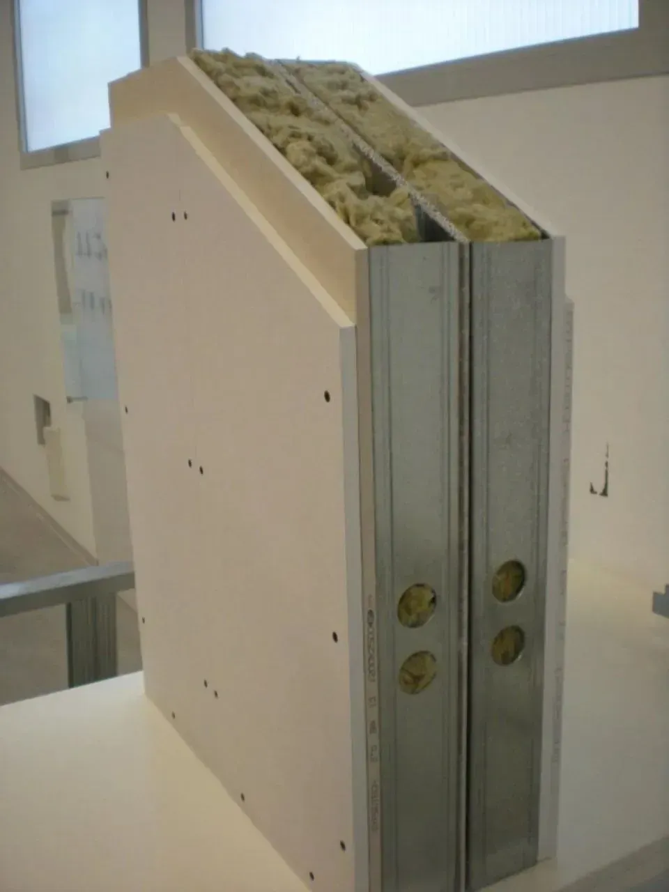 Vista in sezione di una parete che mostra cartongesso, montanti metallici e isolamento.