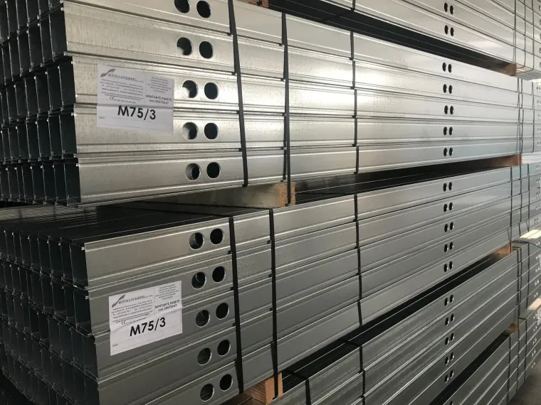 Travi di supporto in acciaio zincato impilate con fori preforati, probabilmente per l'edilizia.