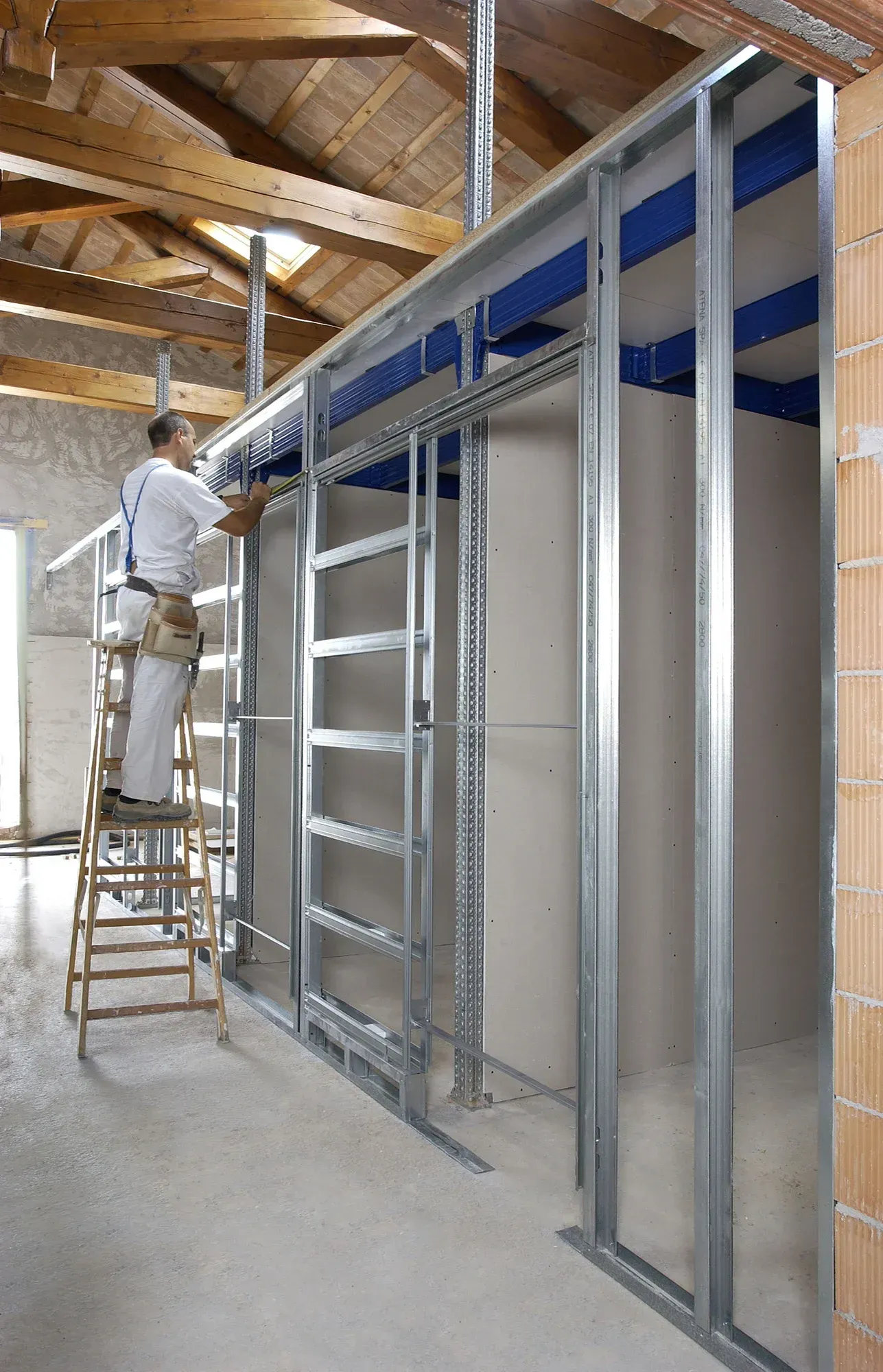 Uomo su una scala che costruisce un muro di metallo con telaio di porta all'interno di un edificio.