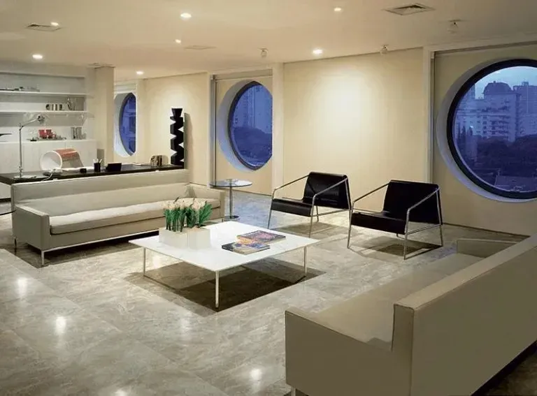 Moderna sala d'attesa per ufficio con divani bianchi, sedie nere, tavolino quadrato e finestre a oblò.