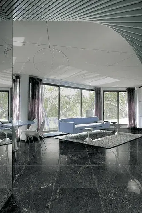 Ampio soggiorno moderno con grandi finestre, divano blu, pavimento piastrellato nero e soffitto curvo.