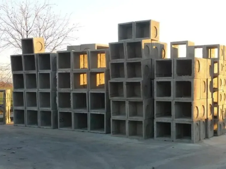 Pile di sezioni quadrate di tombini in cemento grigio all'aperto.