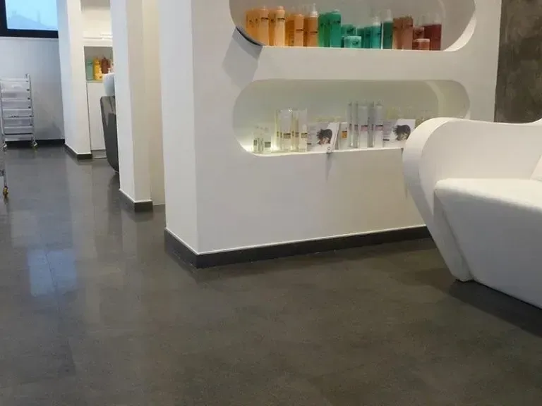 Interno del salone con pareti bianche, scaffali con prodotti, pavimento grigio scuro e divano bianco.