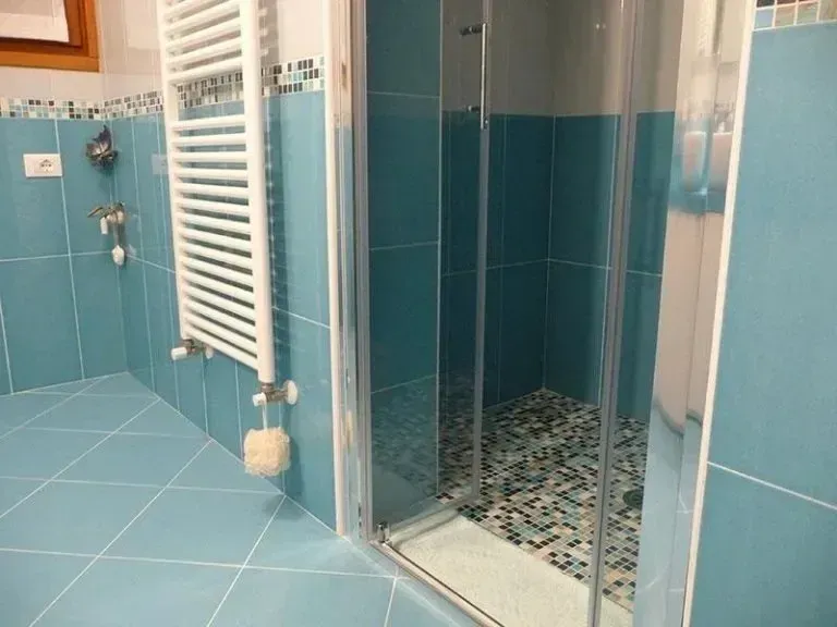 Bagno piastrellato di blu con box doccia in vetro e scaldasalviette bianco.