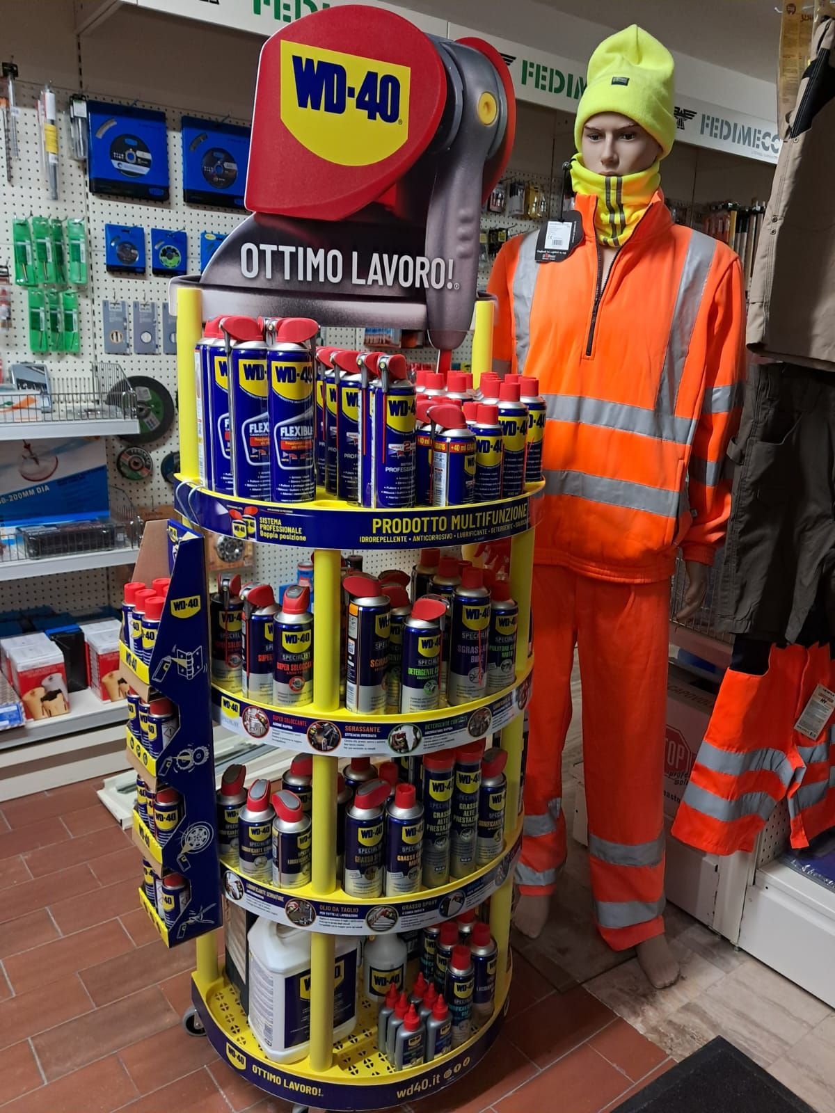 Manichino in abiti da lavoro arancioni accanto a un espositore di prodotti WD-40 in un negozio.