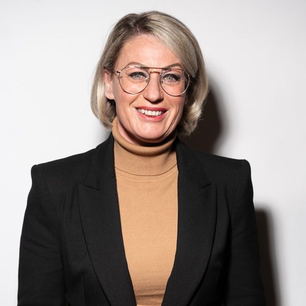 Een vrouw met een bril en een zwart jasje lacht naar de camera