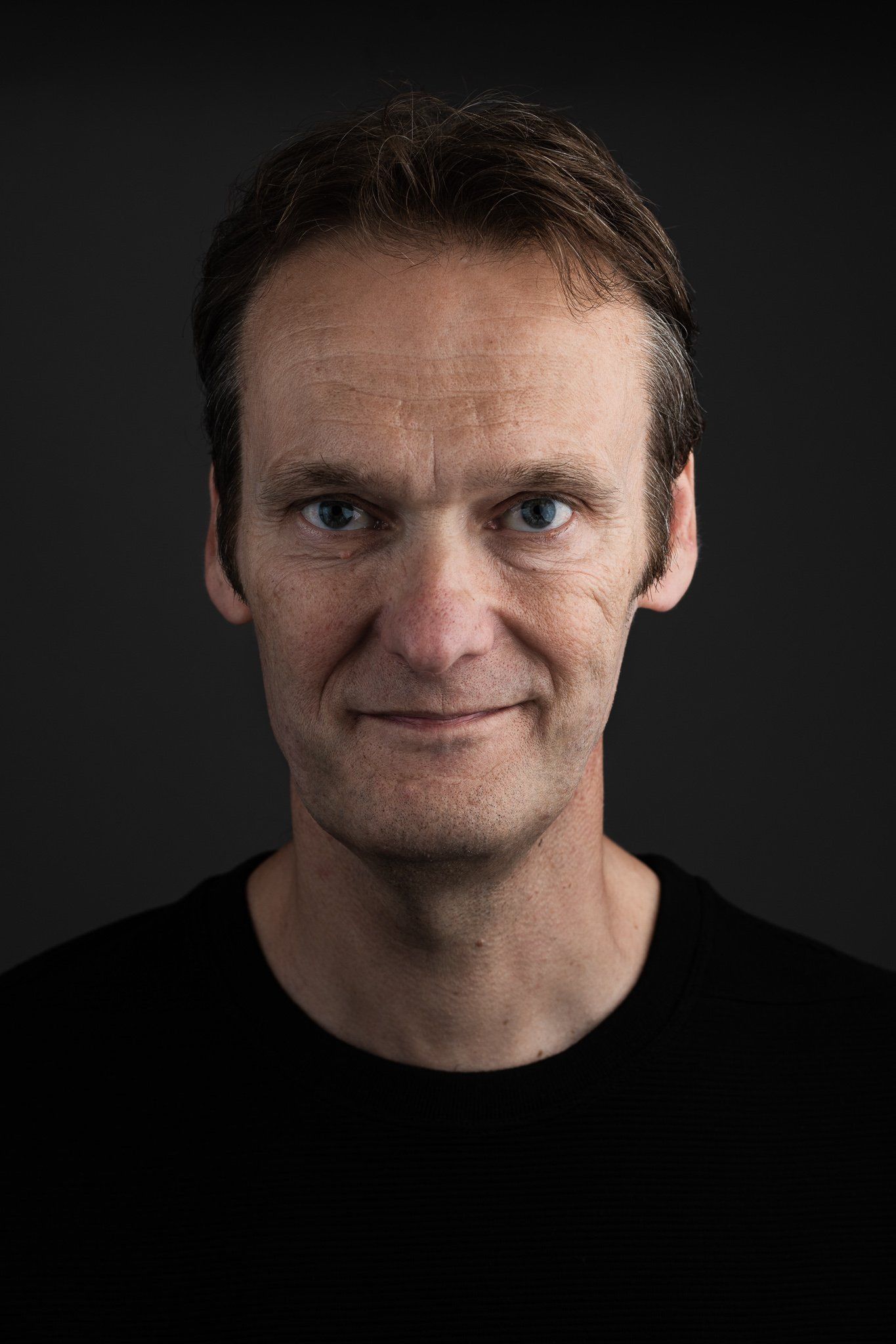 Een man in een zwart shirt lacht naar de camera.