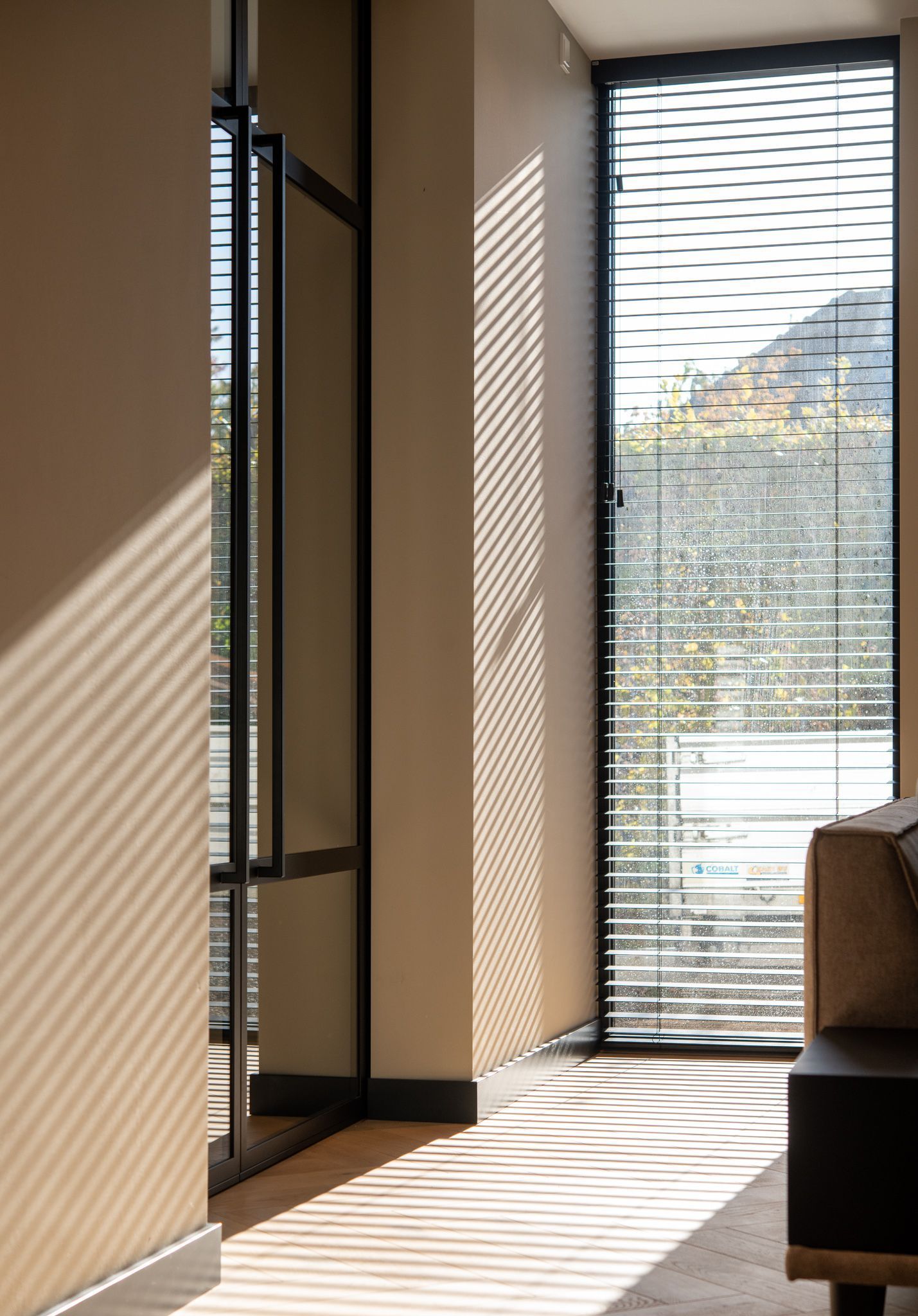 Een woonkamer met een bank en een groot raam met jaloezieën.