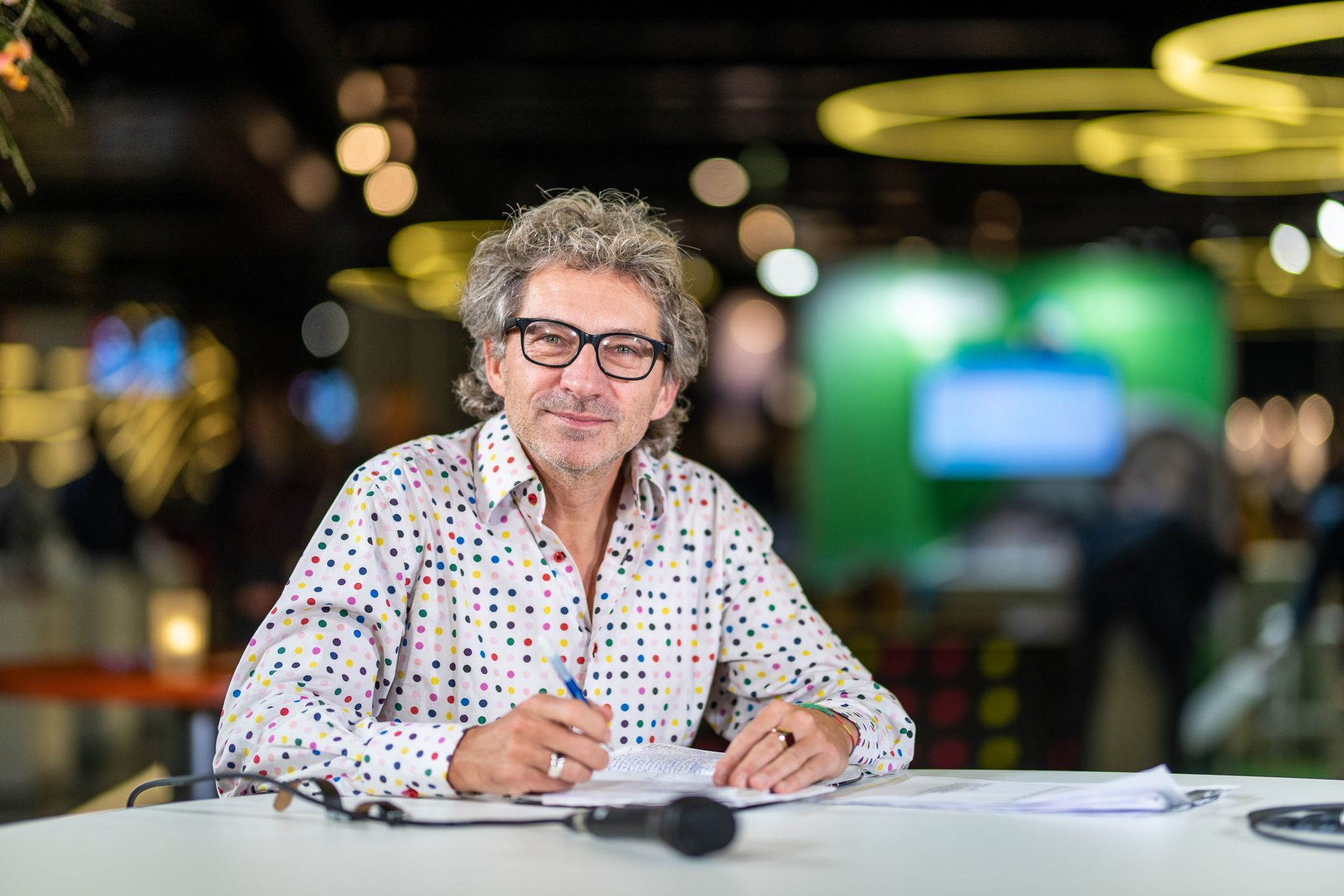 Een man zit aan een tafel met een microfoon en schrijft op een stukje papier.