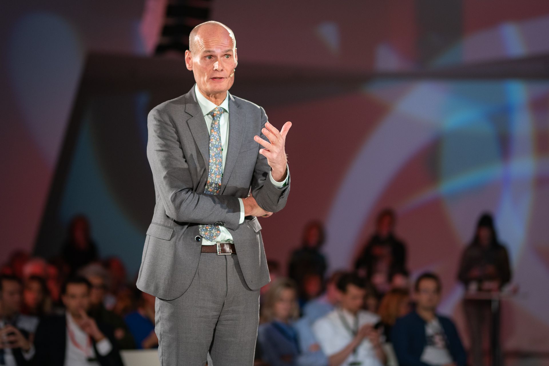 Een man in pak en stropdas staat op een podium en geeft een toespraak.