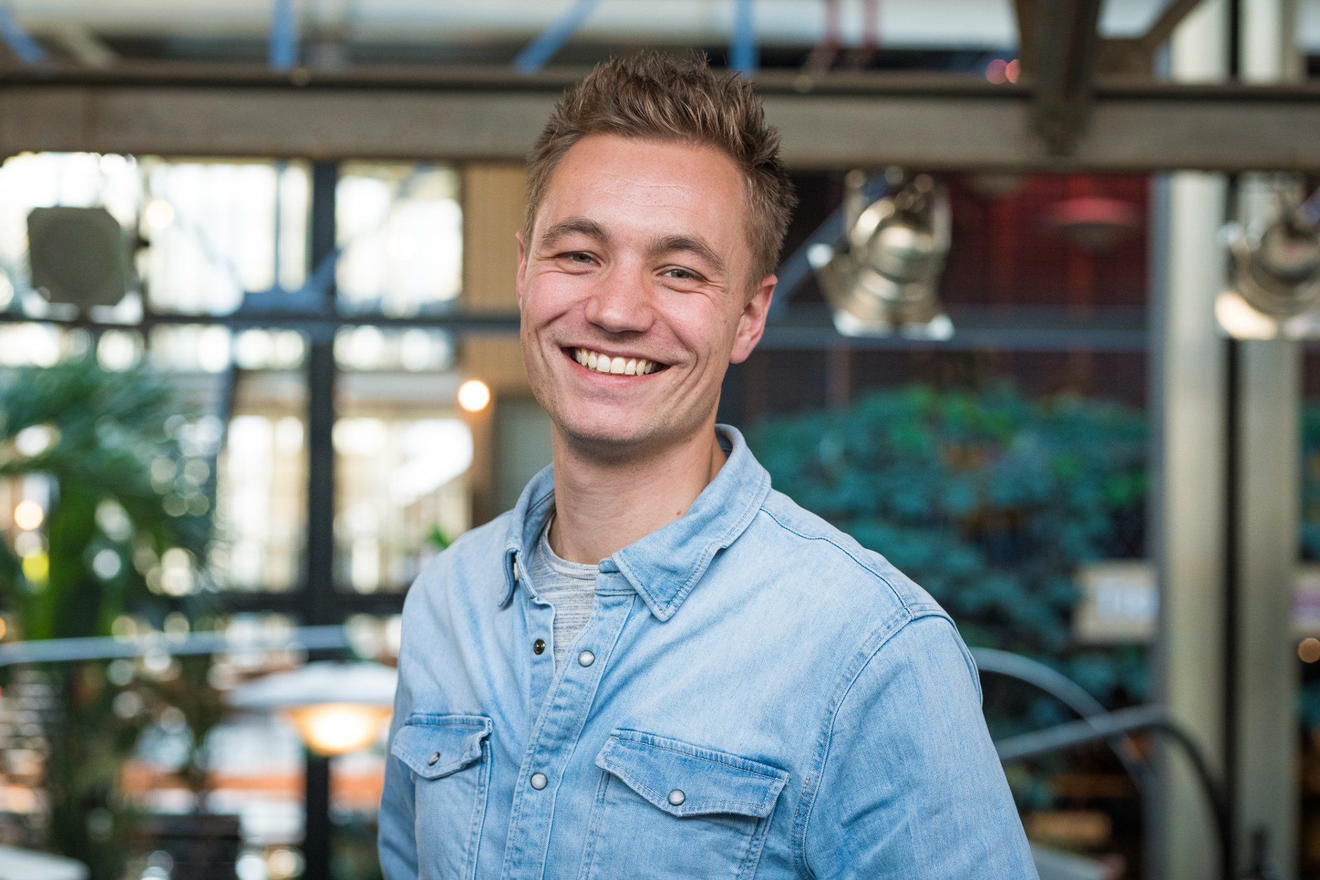 Een jongeman in een spijkerbroek lacht naar de camera.