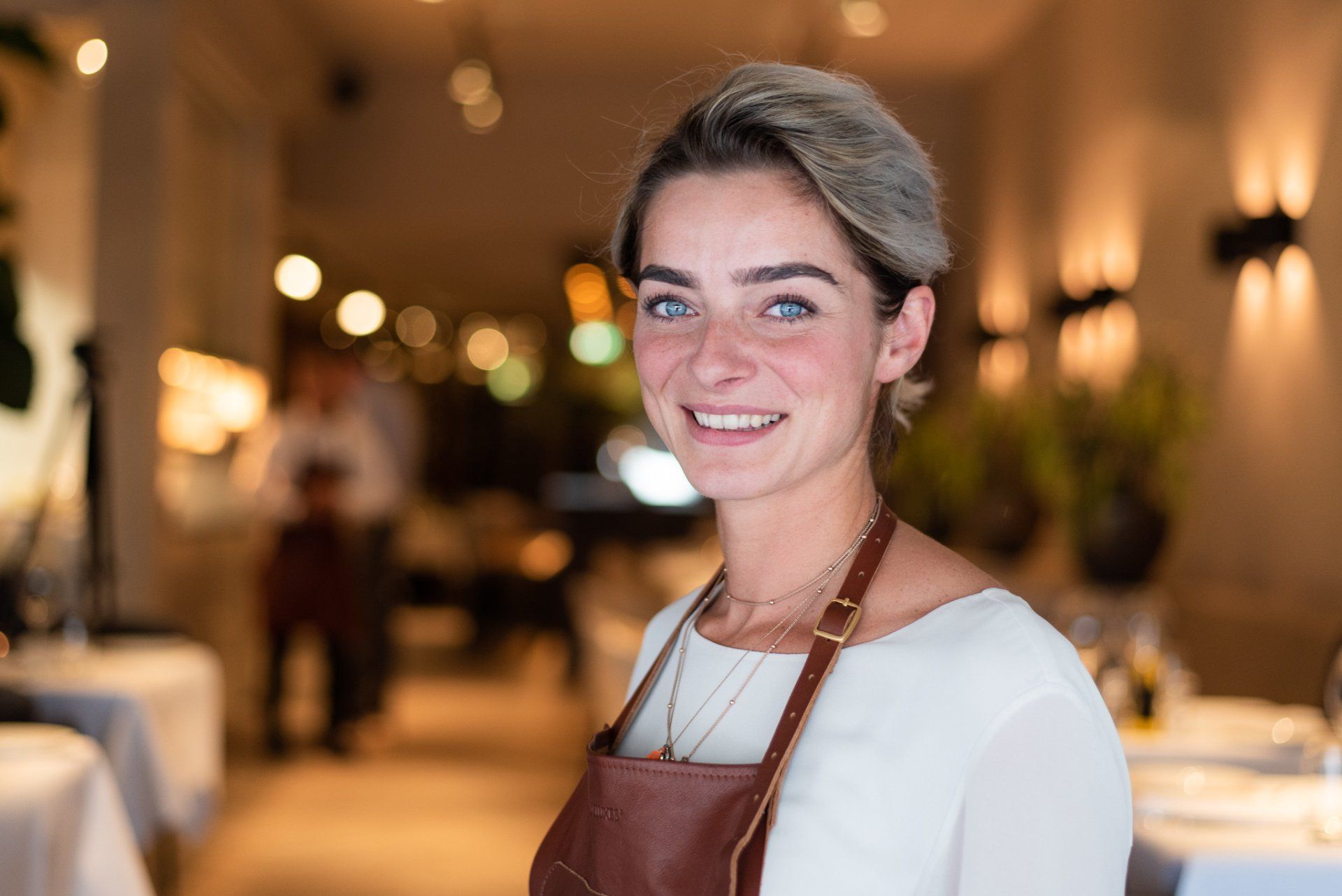 Een vrouw met een schort aan lacht in een restaurant.