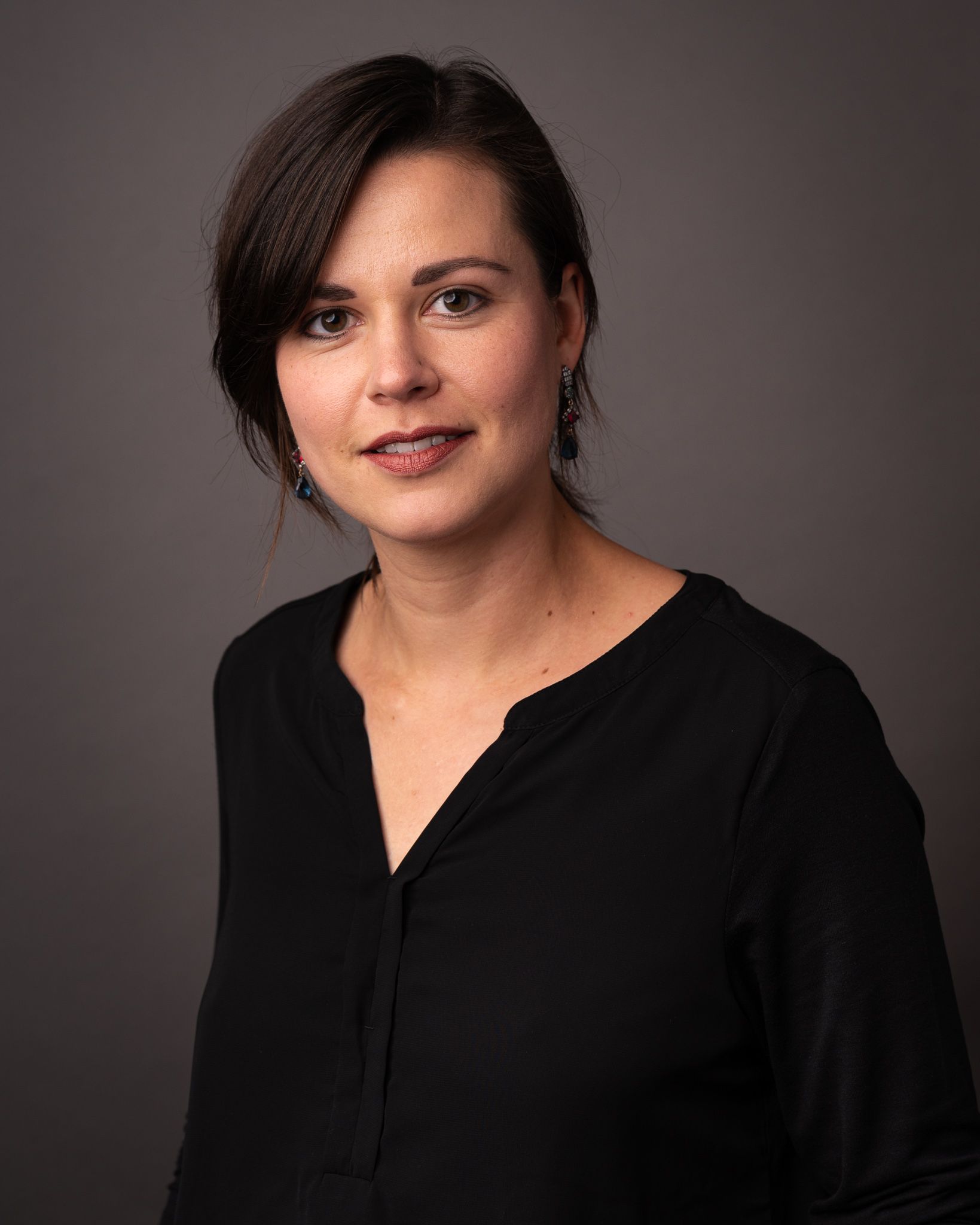 Een vrouw in een zwart shirt staat voor een grijze achtergrond.