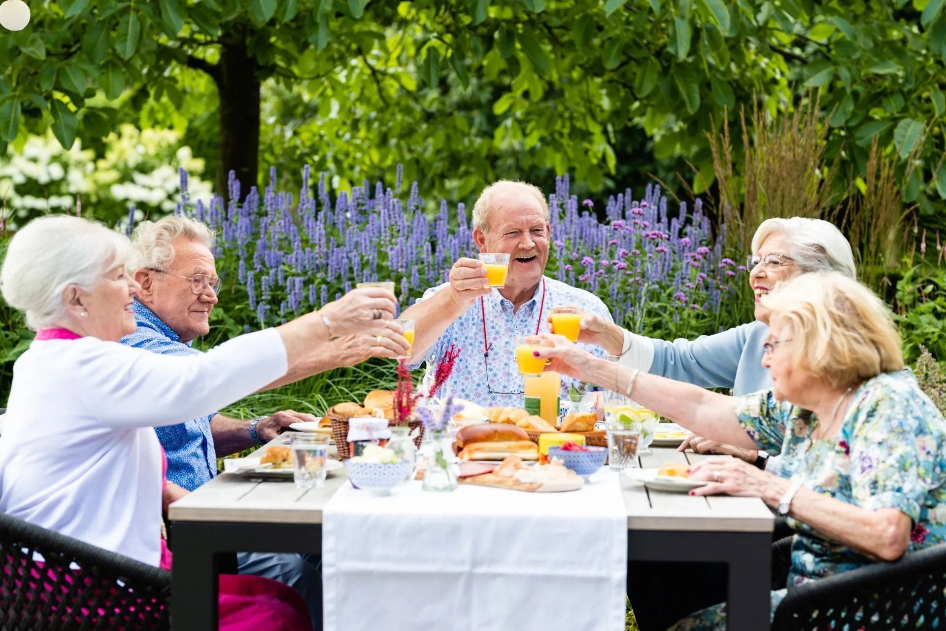 Een groep ouderen zit aan een tafel en proost met een drankje.