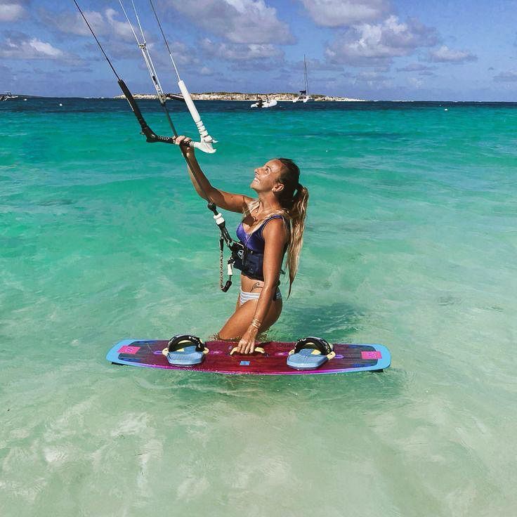 A woman in a bikini is kneeling on a surfboard in the ocean.
