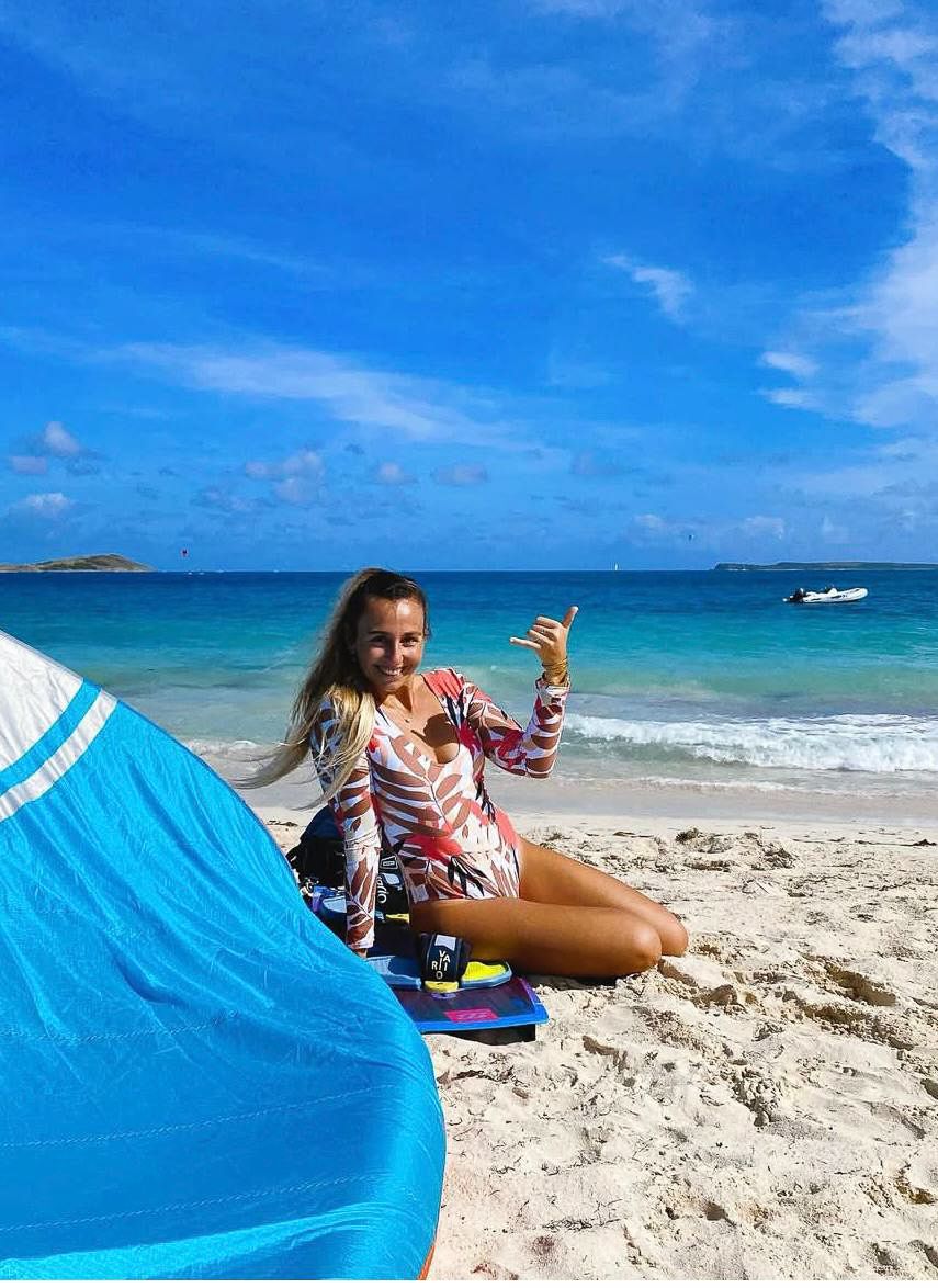 A woman is sitting on the beach next to a blue tent.