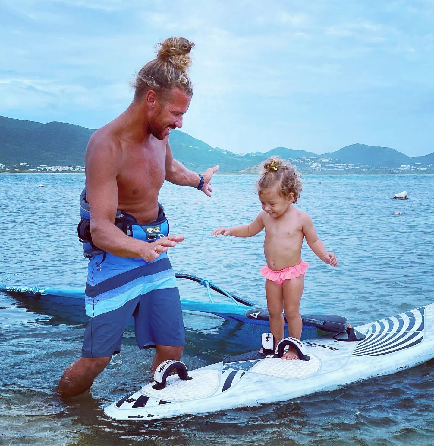 A man and a little girl are standing on a surfboard in the water
