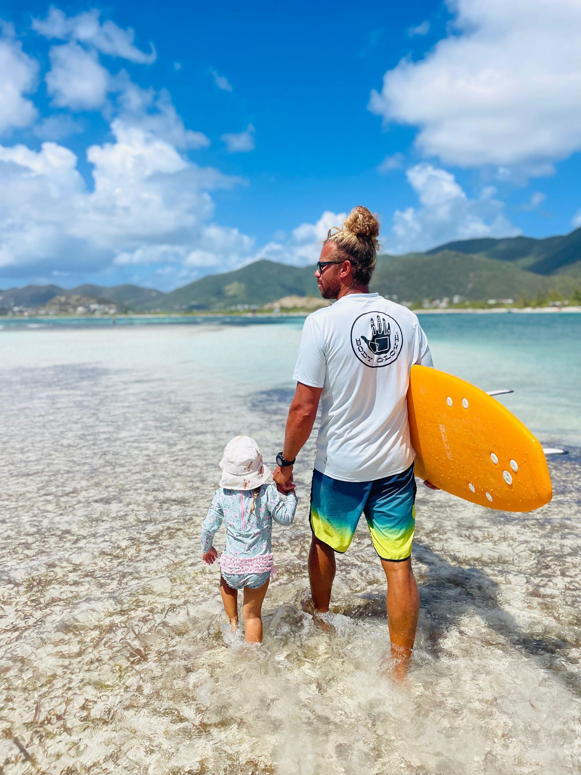 A man is holding a surfboard and a child is walking on the beach.