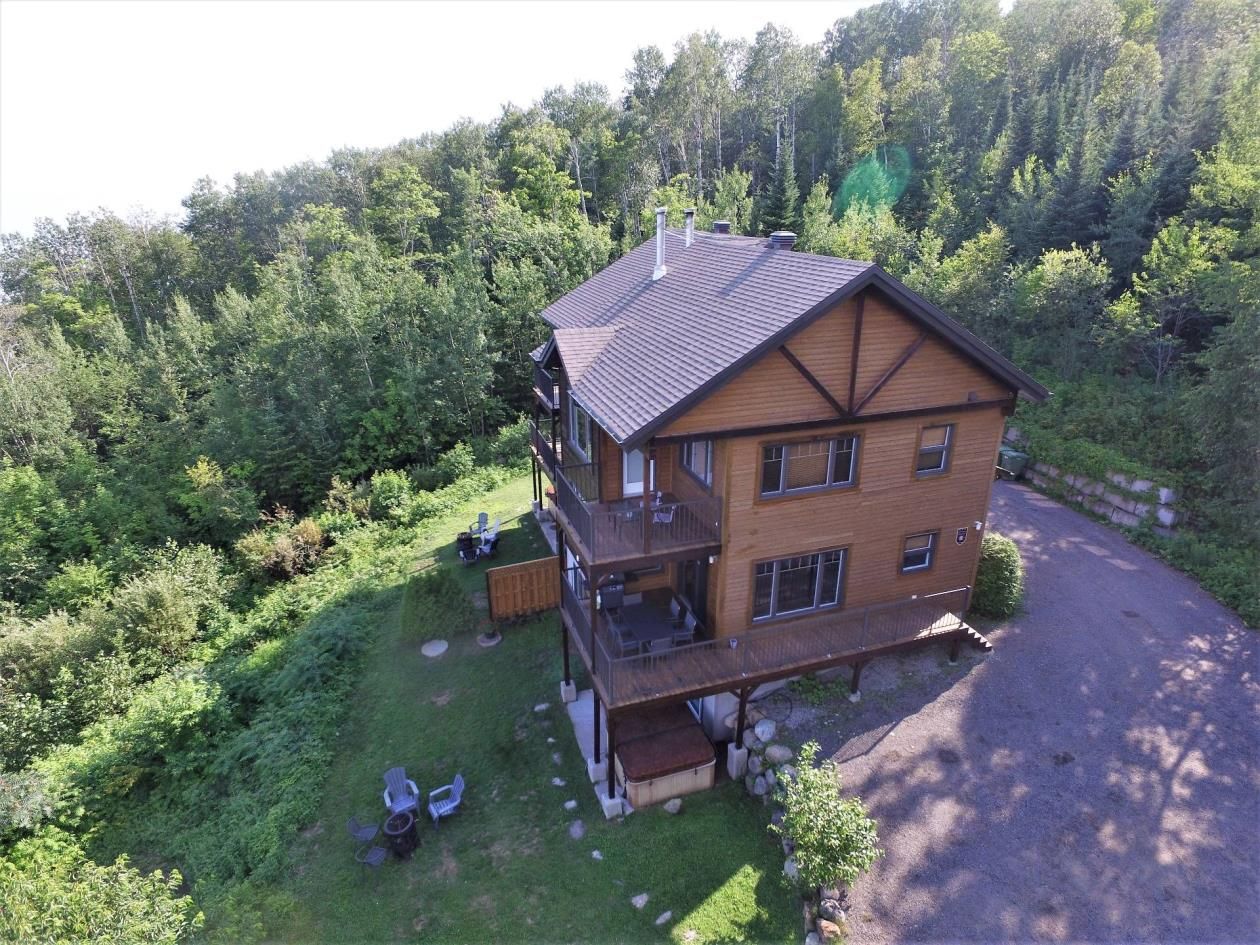 Maison en bois brun avec terrasse, entourée d'arbres à flanc de colline.