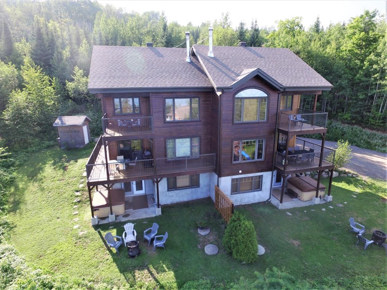 Chalet marron avec plusieurs terrasses, situé dans une zone boisée avec pelouse.