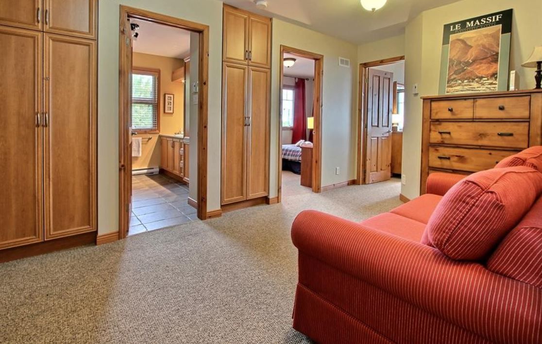 Bedroom with orange couch, doors to bathroom and another room, built-in wooden cabinets.