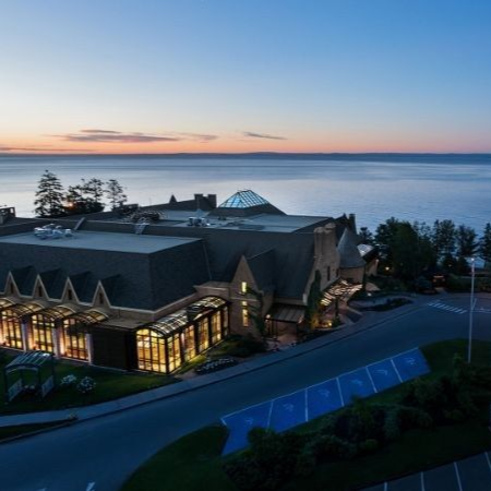 Bâtiment d'hôtel au crépuscule, surplombant un plan d'eau sous un ciel de coucher de soleil.