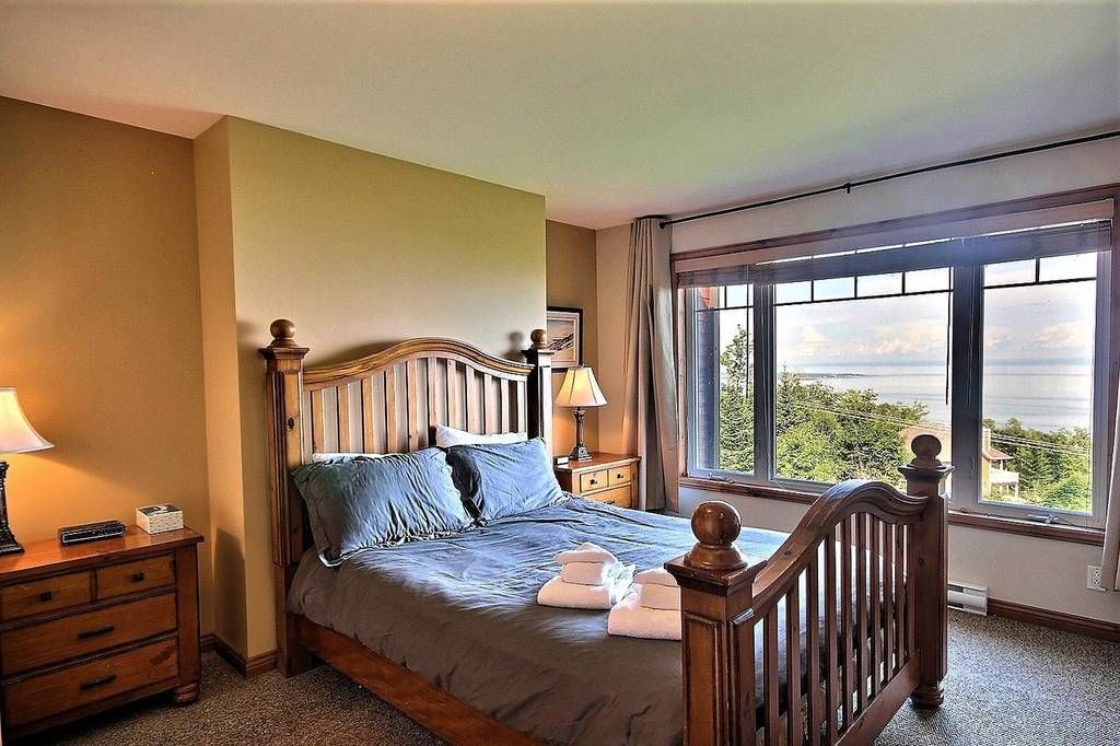 Chambre avec lit en bois, table de chevet et grande fenêtre donnant sur une vue panoramique.