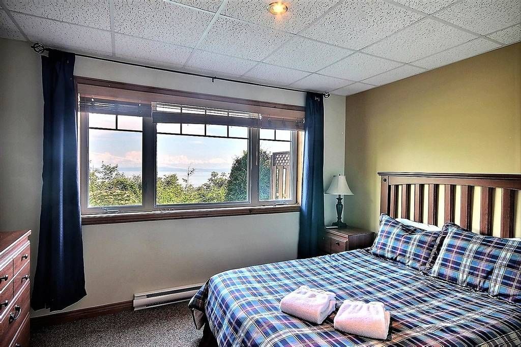 Chambre avec lit, fenêtre avec vue, commode et linge de lit à carreaux bleus.