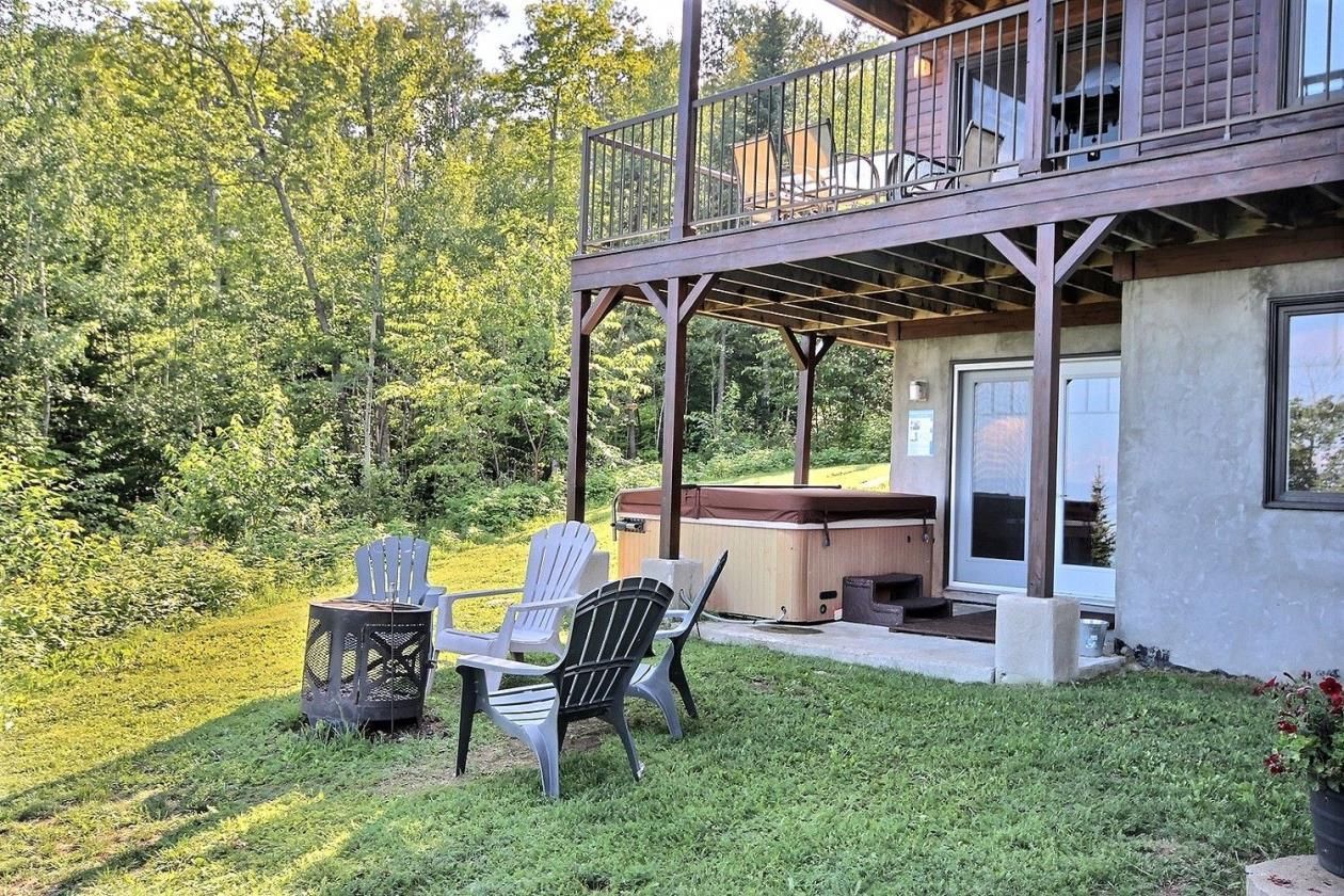 Une maison avec une terrasse donnant sur un jardin aménagé avec des chaises, un foyer extérieur et un bain à remous.
