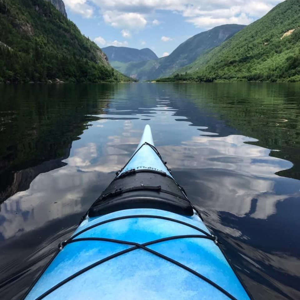 Blue kayak on calm water, surrounded by mountains, reflecting the sky.