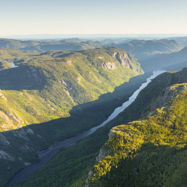 Rivière serpentant à travers un terrain montagneux verdoyant, illuminé par le soleil.