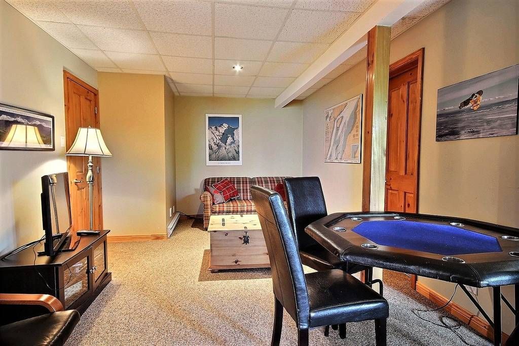 Un sous-sol aménagé avec une table de poker, un canapé, une télévision et des œuvres d'art. Murs marron, moquette beige.