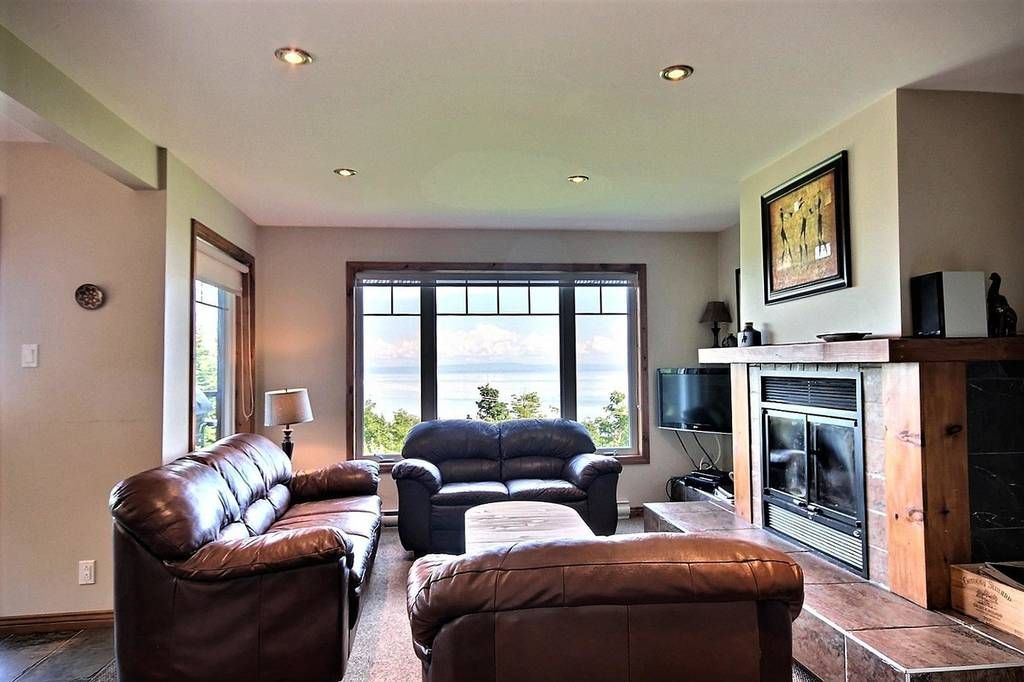 Salon avec canapés en cuir, cheminée et grande fenêtre donnant sur l'eau.