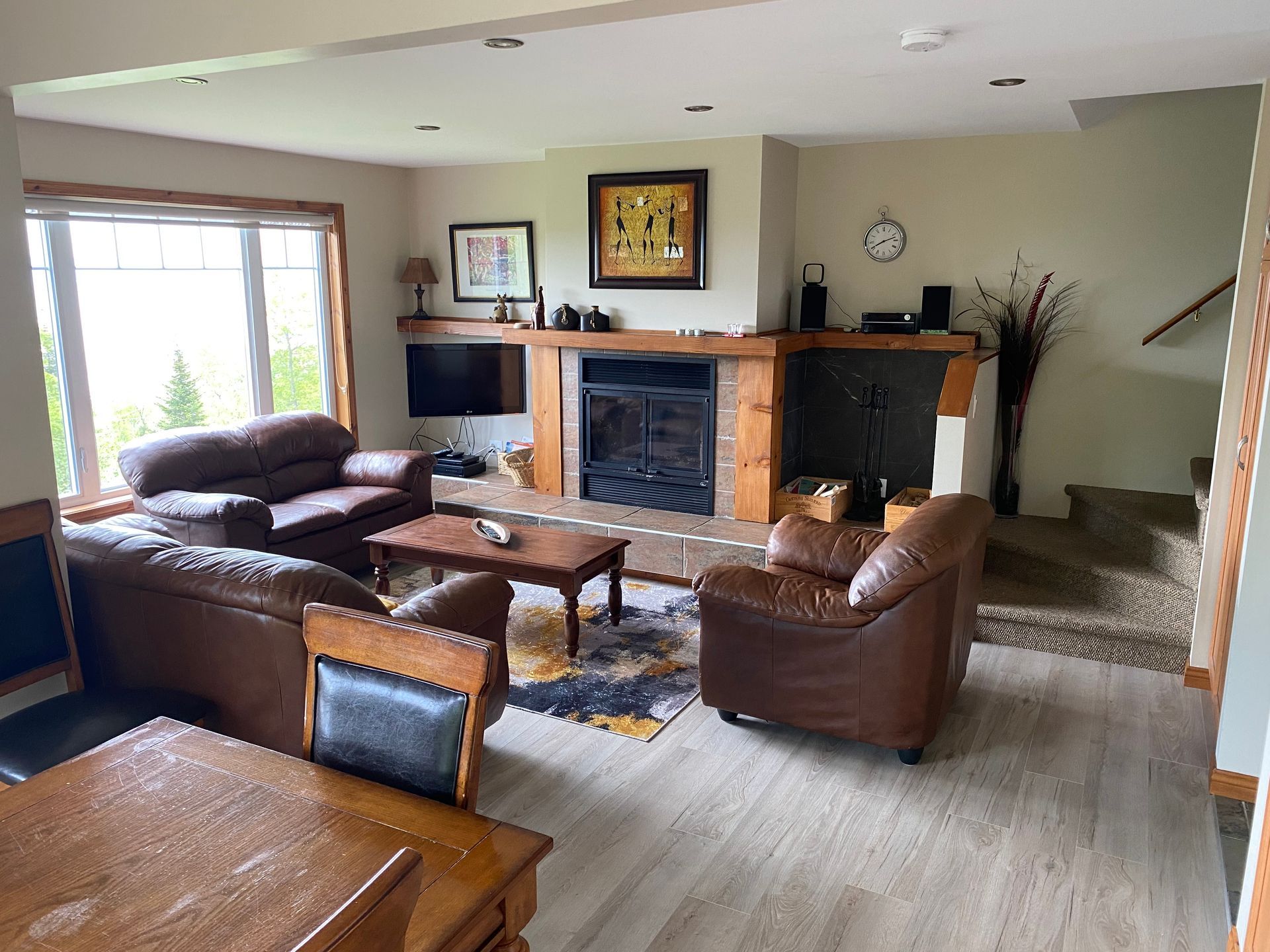 Salon avec meubles en cuir marron, cheminée et fenêtre donnant sur l'extérieur.