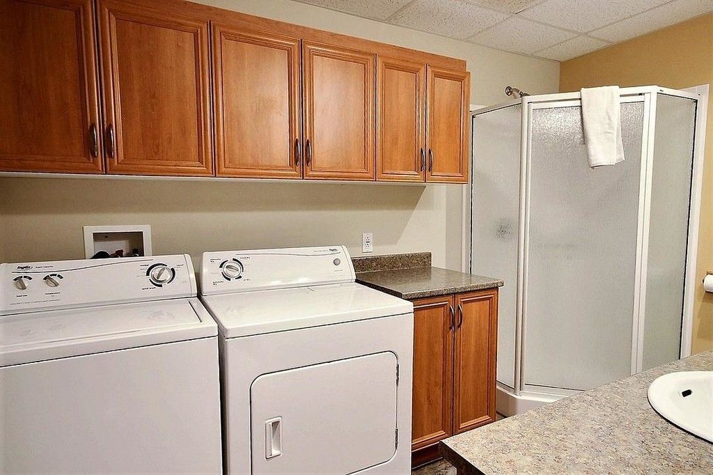 Buanderie avec lave-linge, sèche-linge, placards et douche.