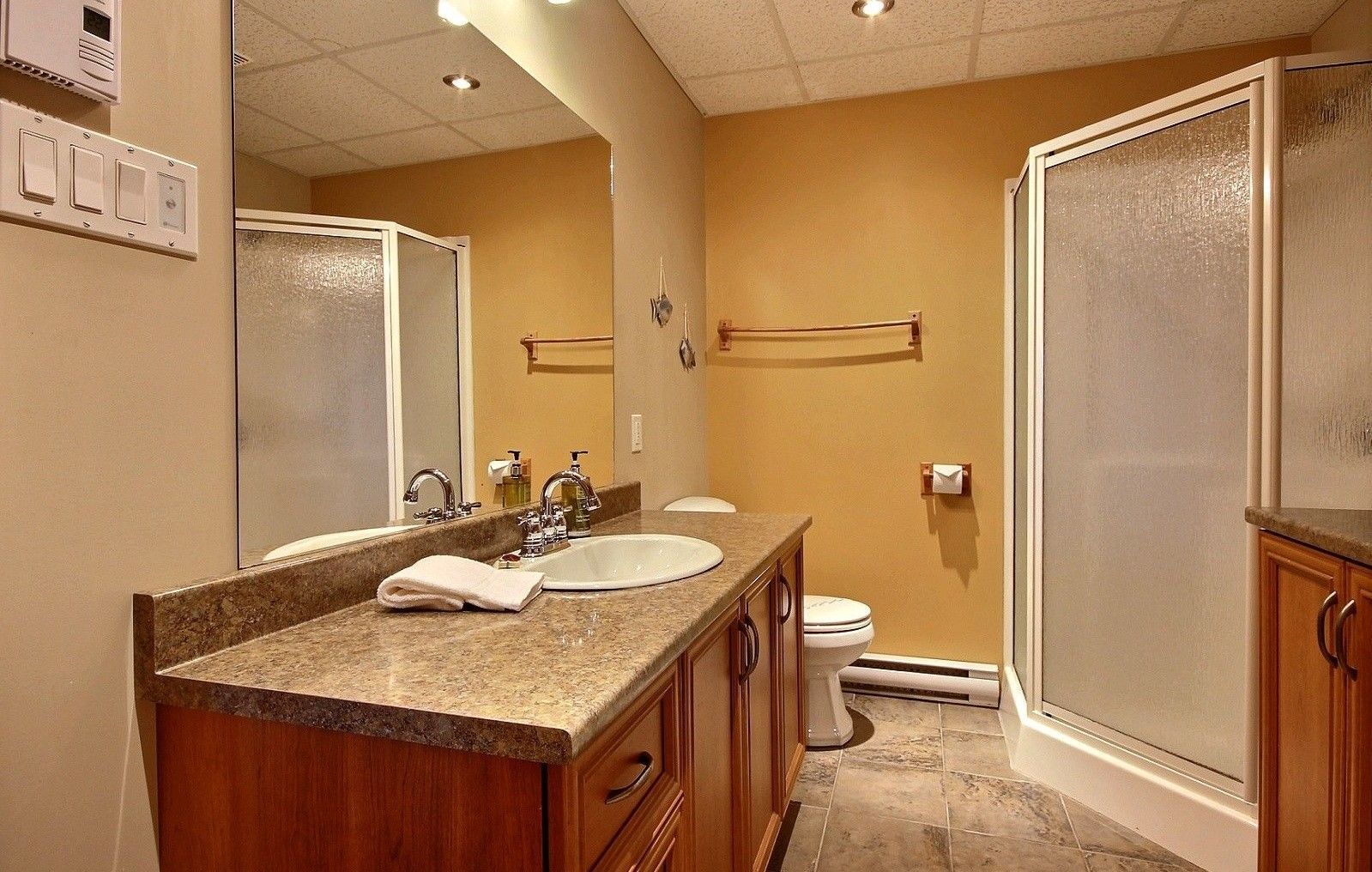 Salle de bains avec meubles marron, murs beiges et douche avec portes en verre dépoli.