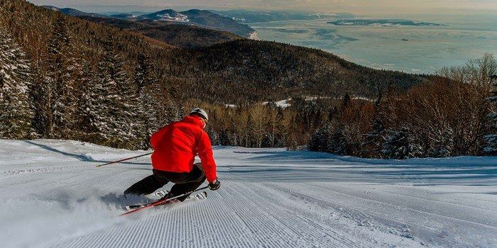 Un skieur en veste rouge dévale une pente enneigée en direction d'un lac brumeux au loin.
