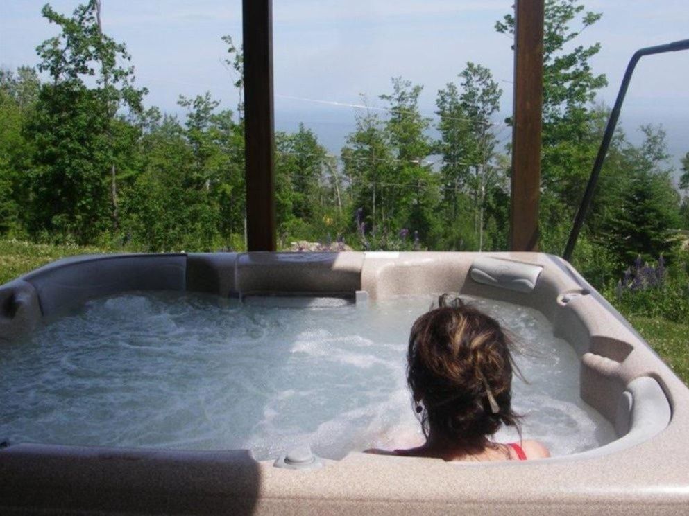 Femme dans un jacuzzi avec vue sur une forêt et un plan d'eau.