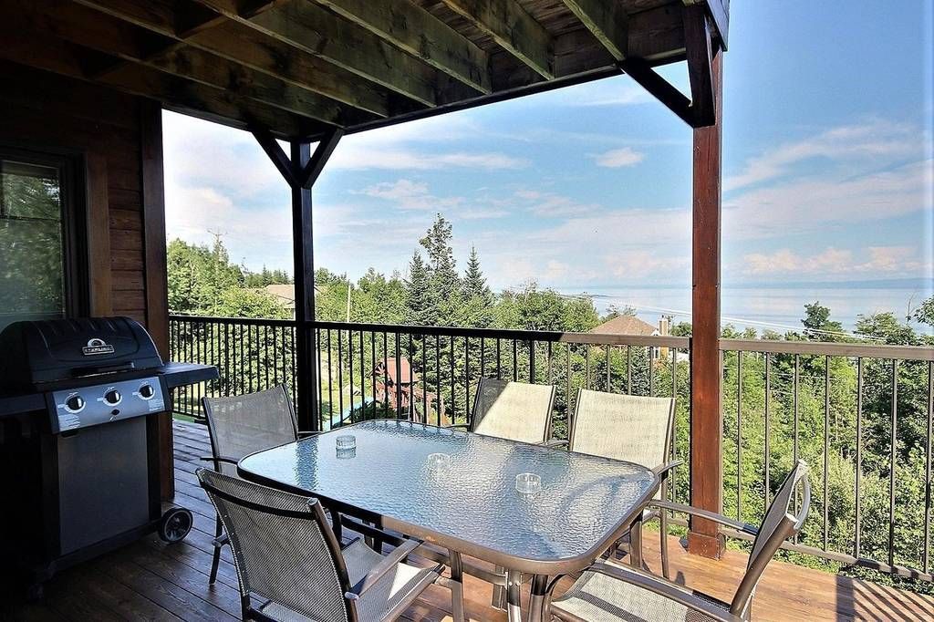 Terrasse avec table, chaises, barbecue et vue panoramique sur les arbres et le ciel.
