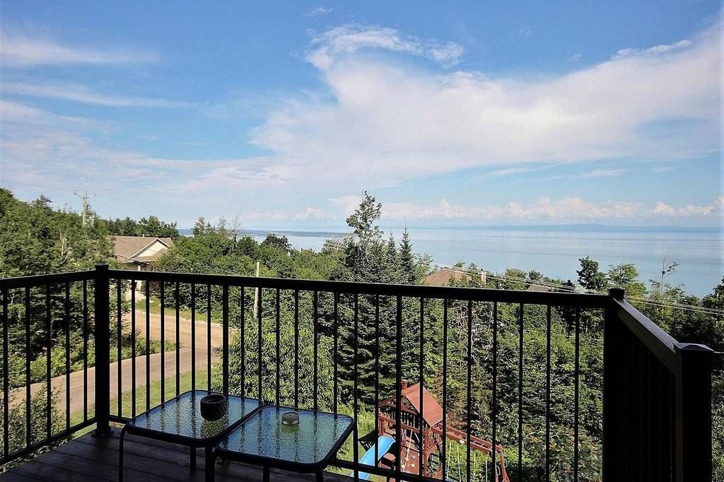 Balcon donnant sur un plan d'eau et une lisière de forêt, sous un ciel bleu.