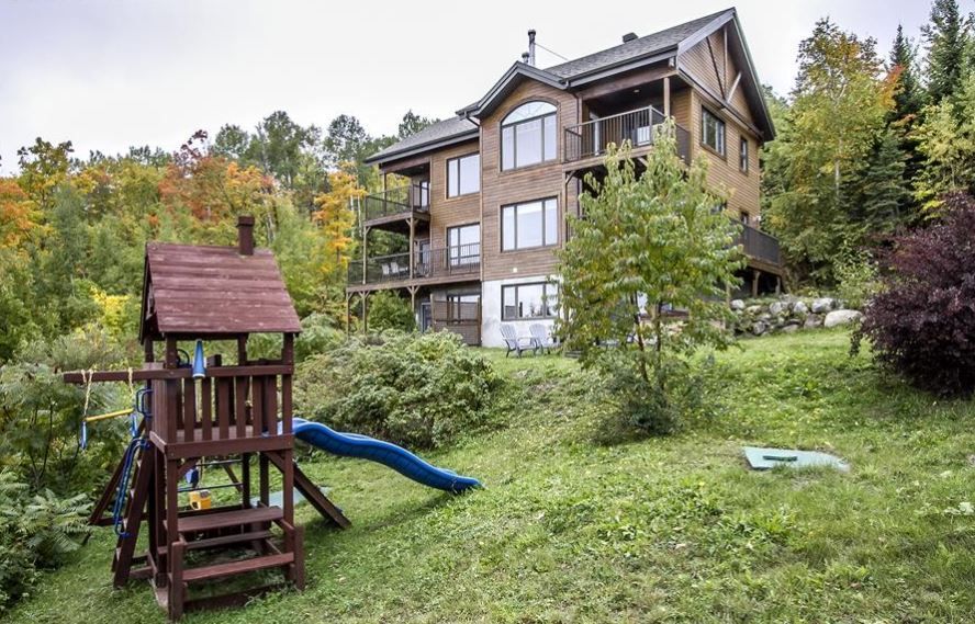 Maison brune de trois étages avec balcons, une aire de jeux dans la cour, nichée dans une forêt aux couleurs d'automne.