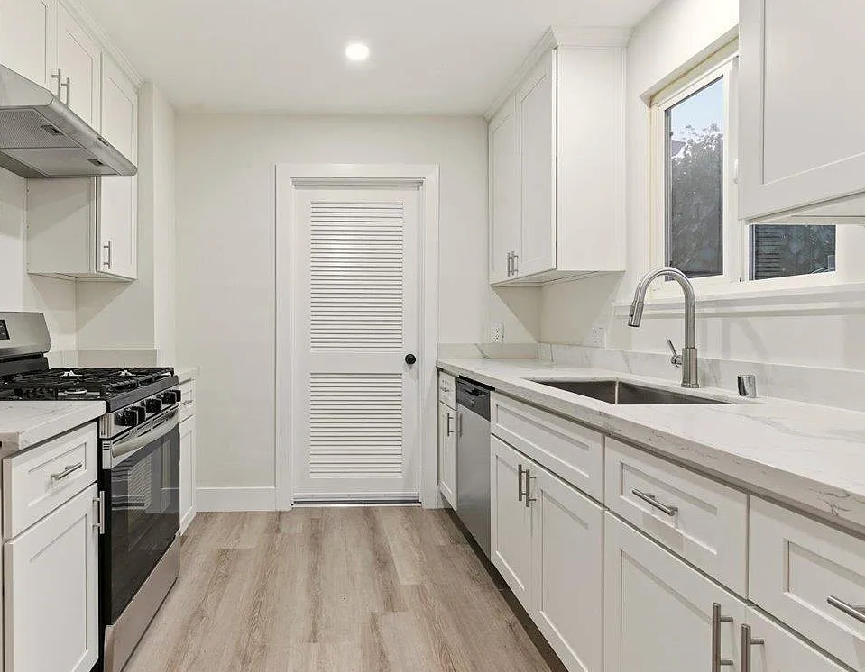 Bright white kitchen with cabinets, stainless steel appliances, and a door with horizontal slats.