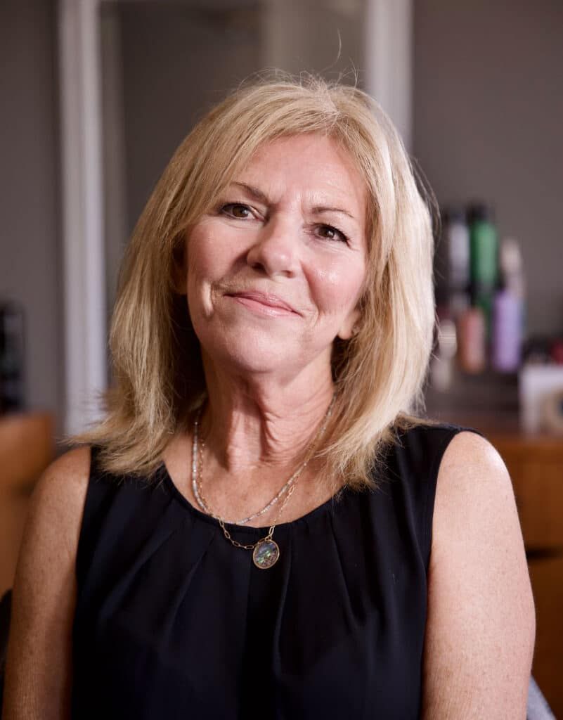 Blond woman in black sleeveless top, smiling, looking at the camera.