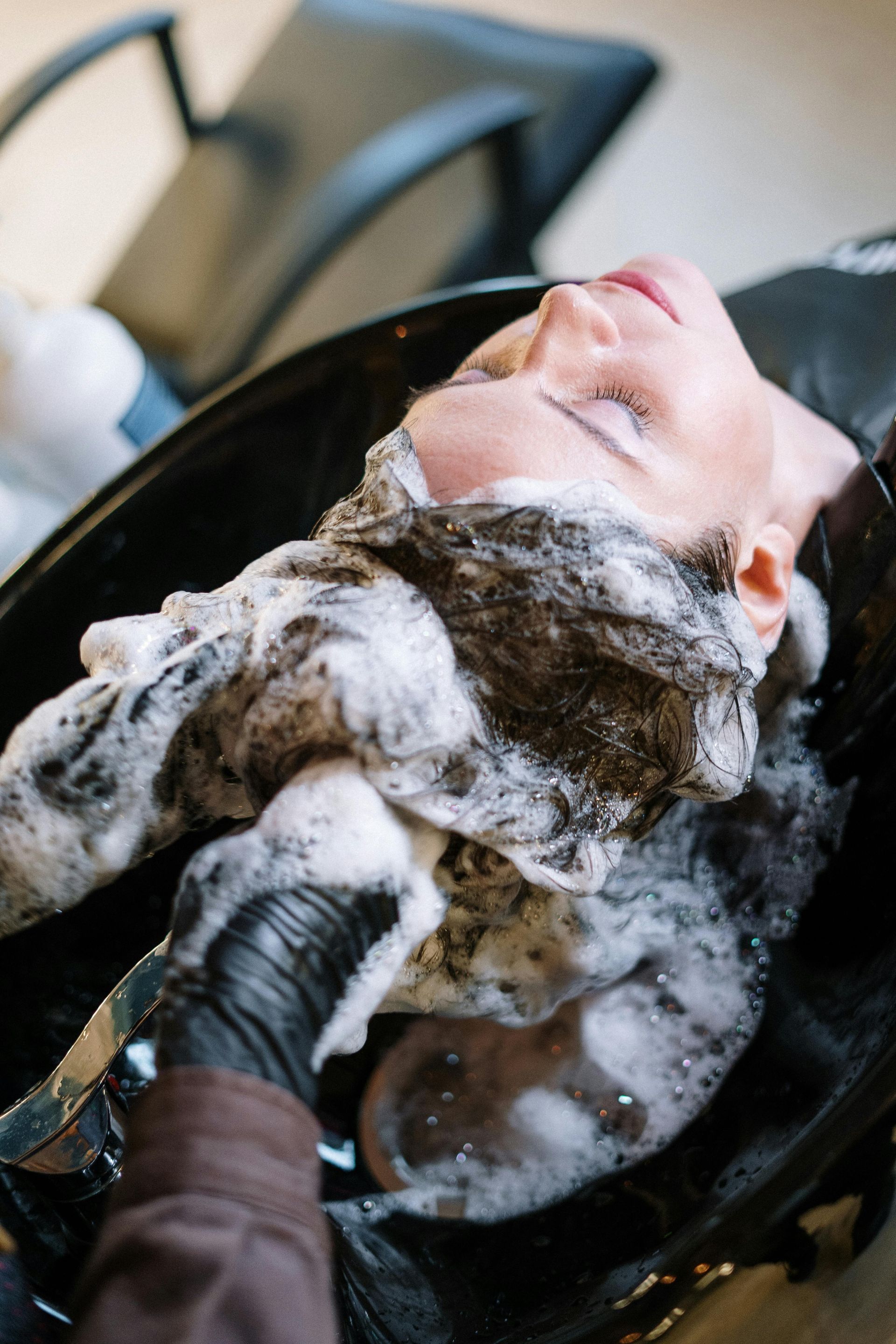 Person getting hair washed in a salon sink, with black gloved hands in view.