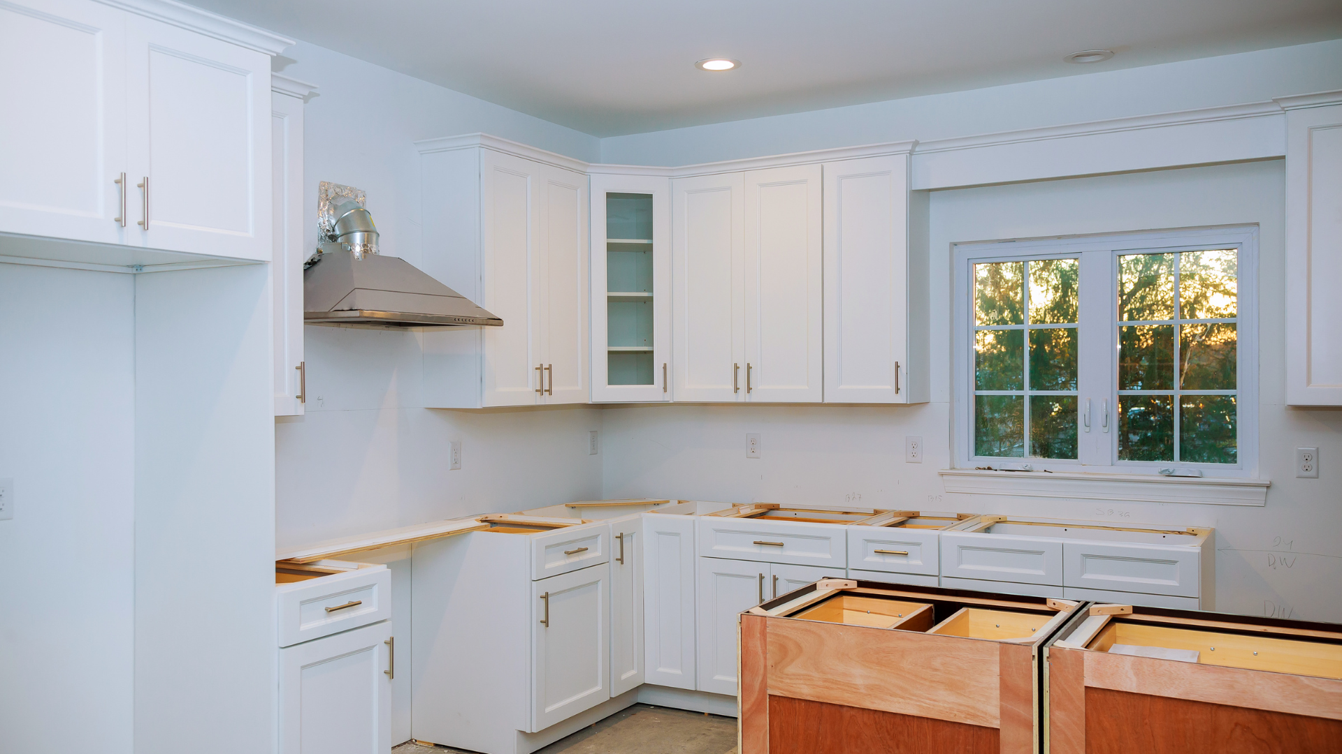 A kitchen under construction with white cabinets and a window.