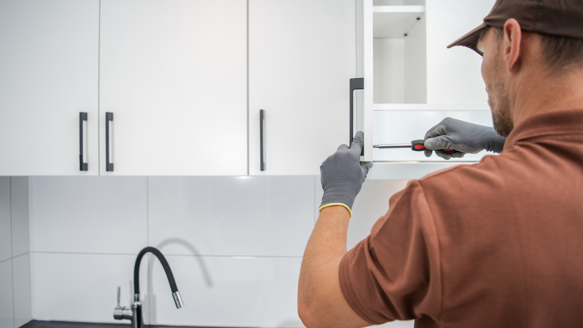 A man is fixing a kitchen cabinet with a screwdriver.